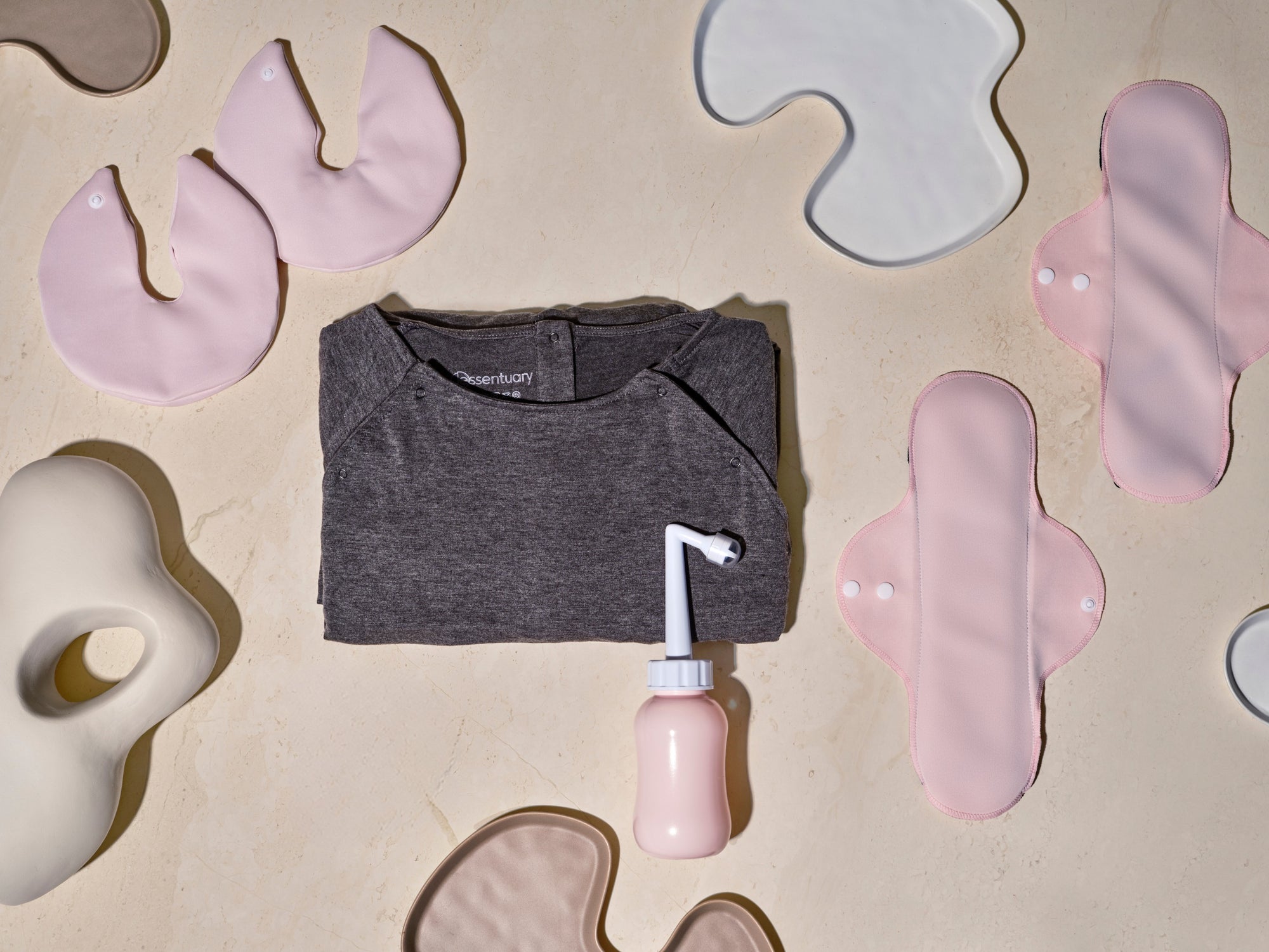 Overzicht van Essentuary postpartum essentials voor in elk vluchtkoffer, met de bostkompressen, Peri Bottle, kraamverband en de bevallingsjurk