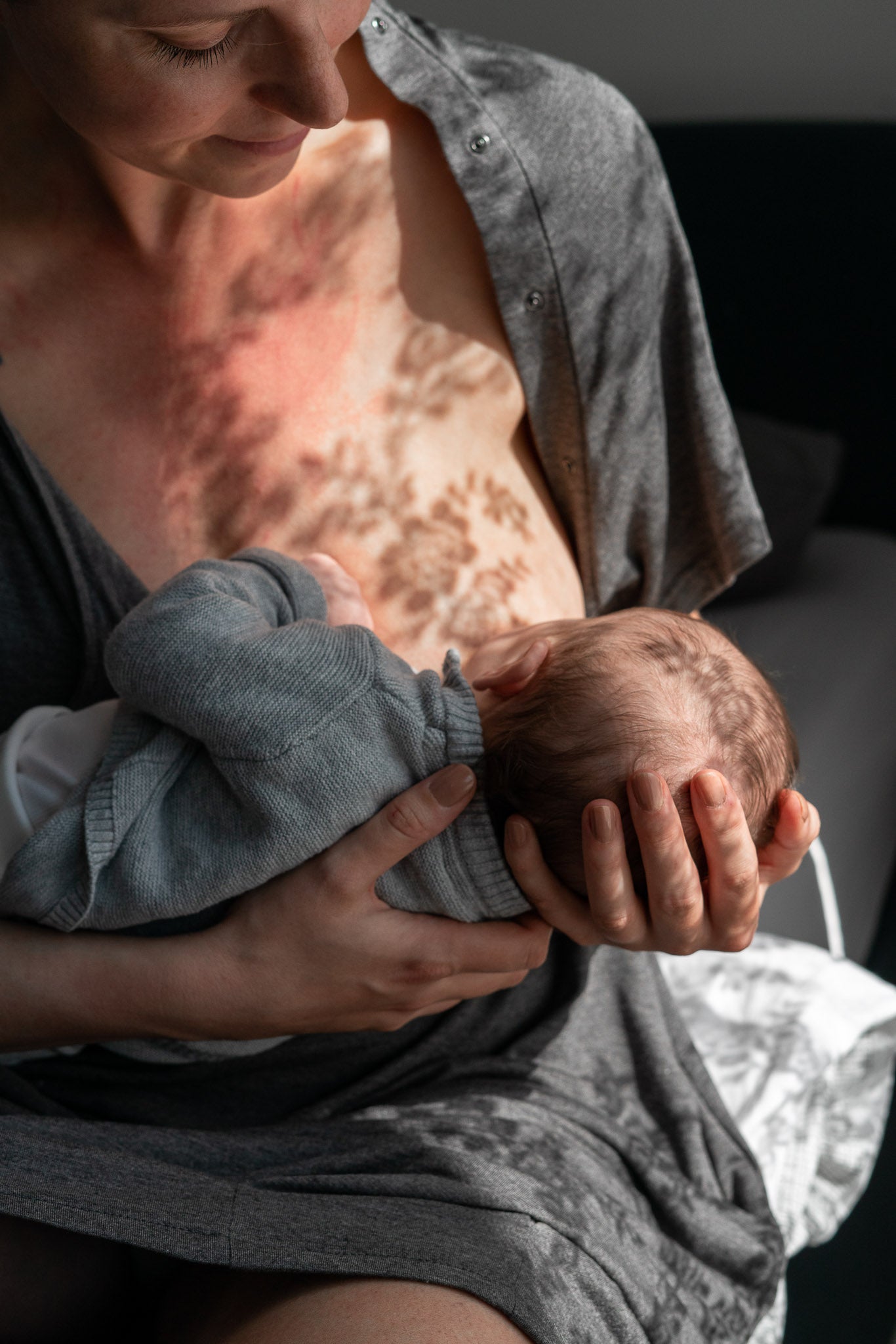 Moeder geeft borstvoeding terwijl ze de grijze bevallingsjurk en voedingsjurk draagt