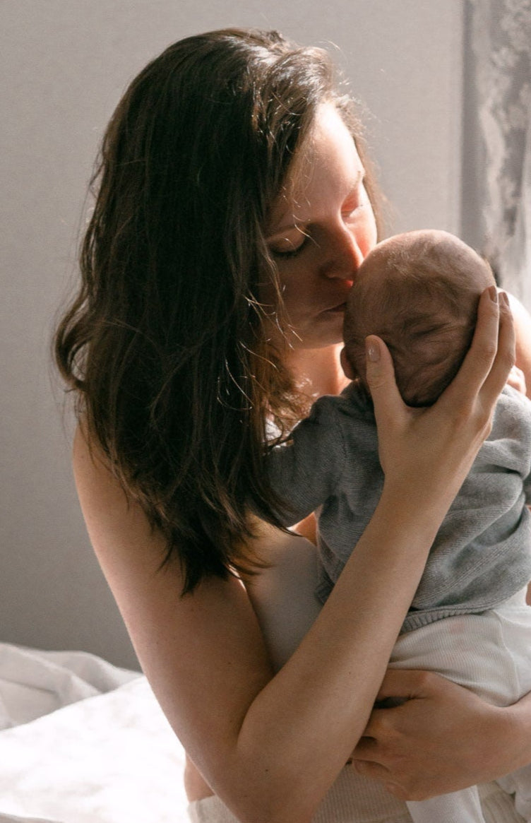 Kraamvrouw met jonge baby geeft kus op een kraambed